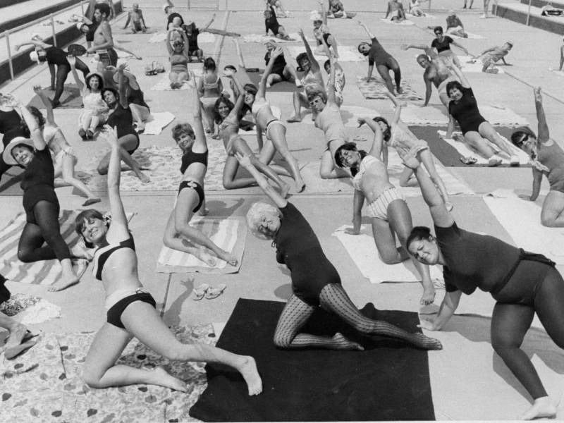 A large exercise class on mats, in black and white