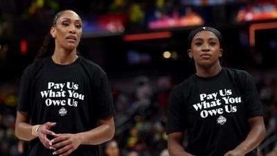 Two WNBA players in black "Pay Us What You Owe Us" shirts