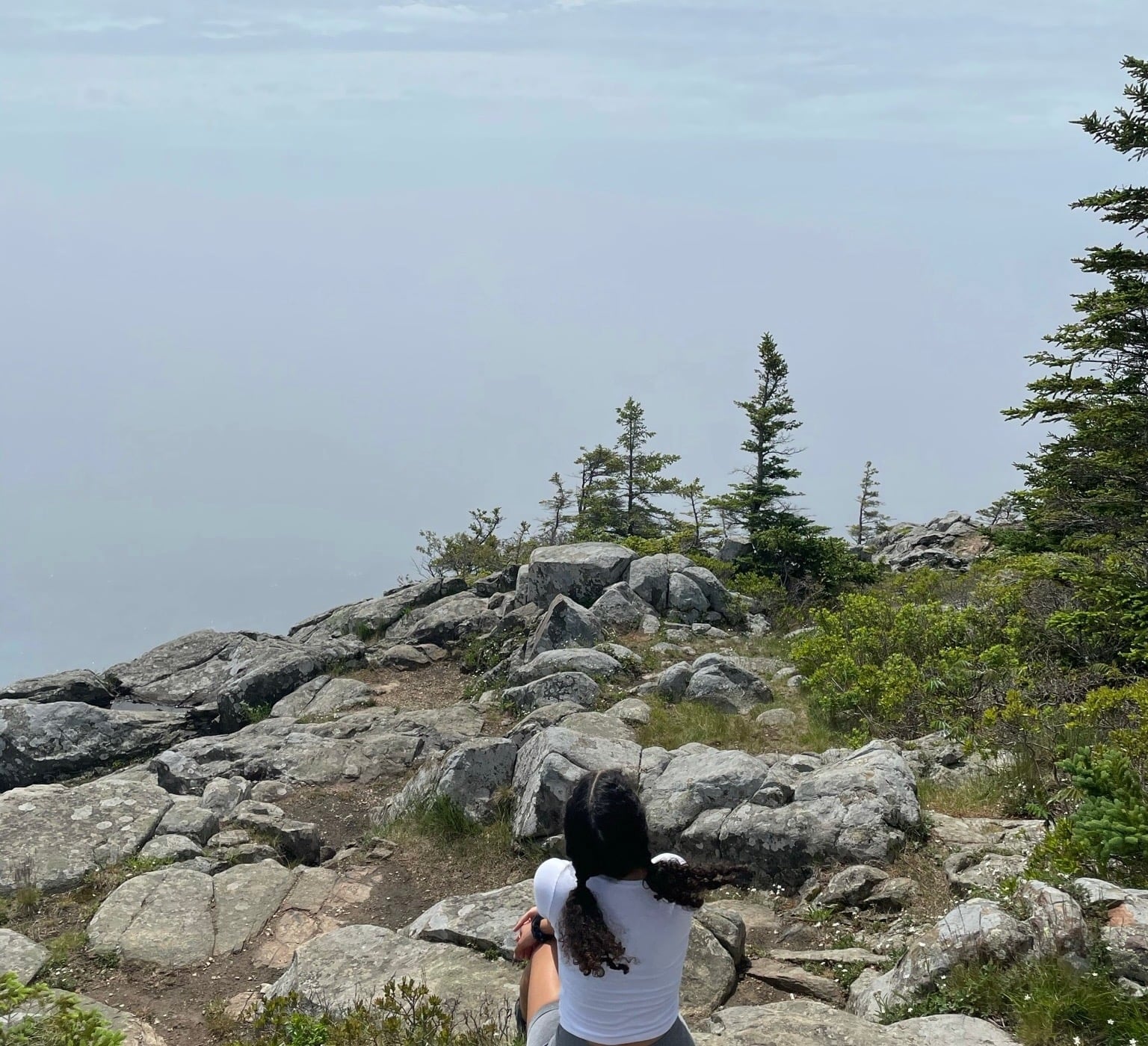 A woman sitting on a rocky summit looking out over misty water