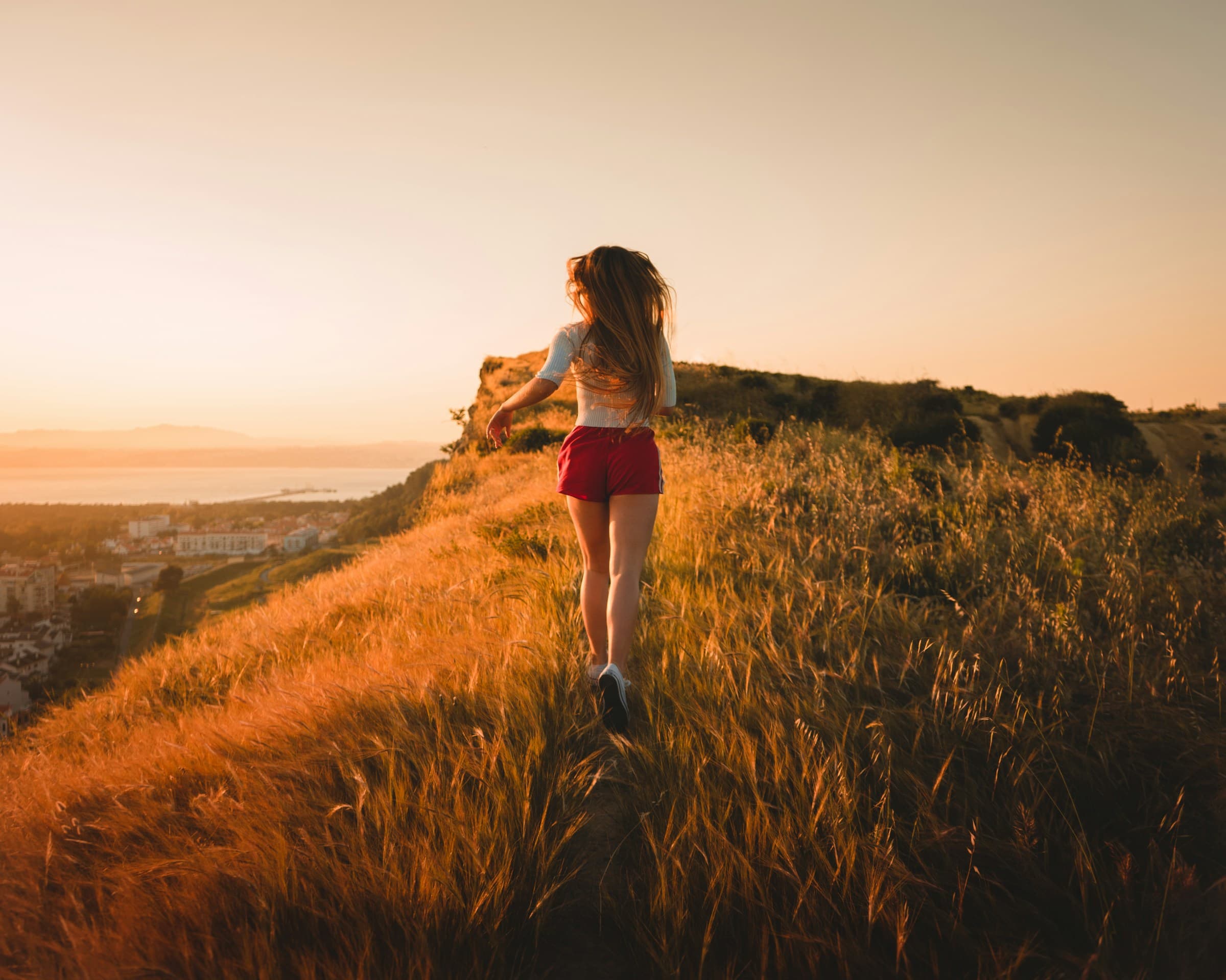 Woman running up a grassy hill in golden evening light